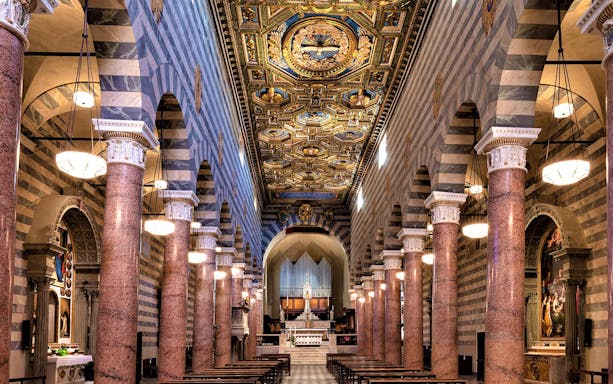 Volterra Duomo interior with ornate ceiling and marble columns.