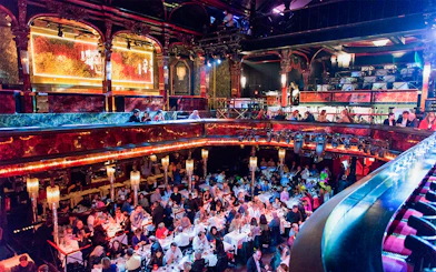 Guests dining in the vibrant hall at Paradis Latin, Paris, with ornate decor and chandeliers.