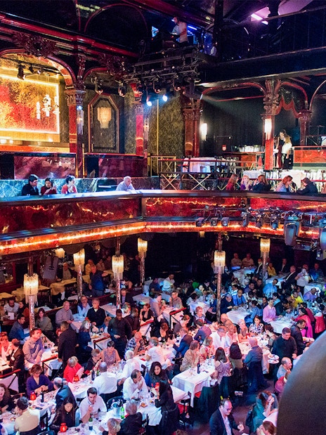 Guests dining in the vibrant hall at Paradis Latin, Paris, with ornate decor and chandeliers.