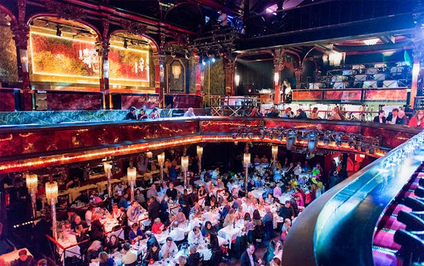 Guests dining in the vibrant hall at Paradis Latin, Paris, with ornate decor and chandeliers.