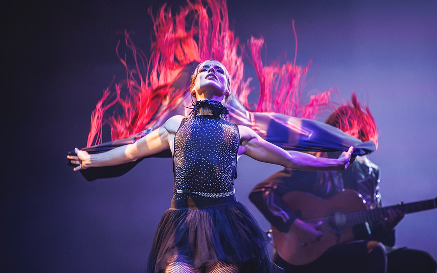 Performer in dynamic dance with flowing red fabric, guitarist in background, WAH show.