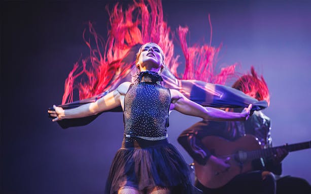 Performer in dynamic dance with flowing red fabric, guitarist in background, WAH show.