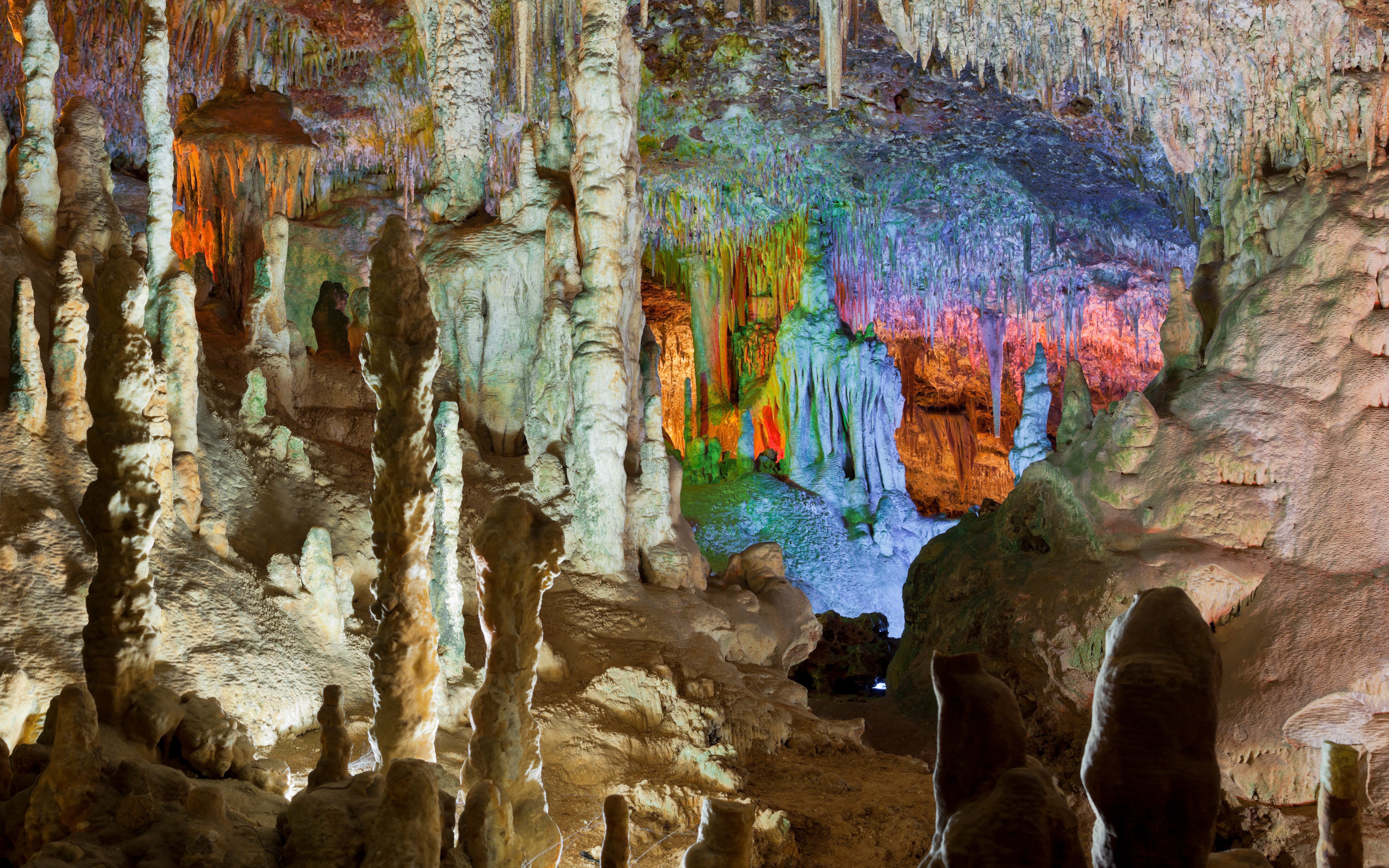 Stalactites and stalagmites inside Drach Caves, Mallorca, illuminated with colorful lights.