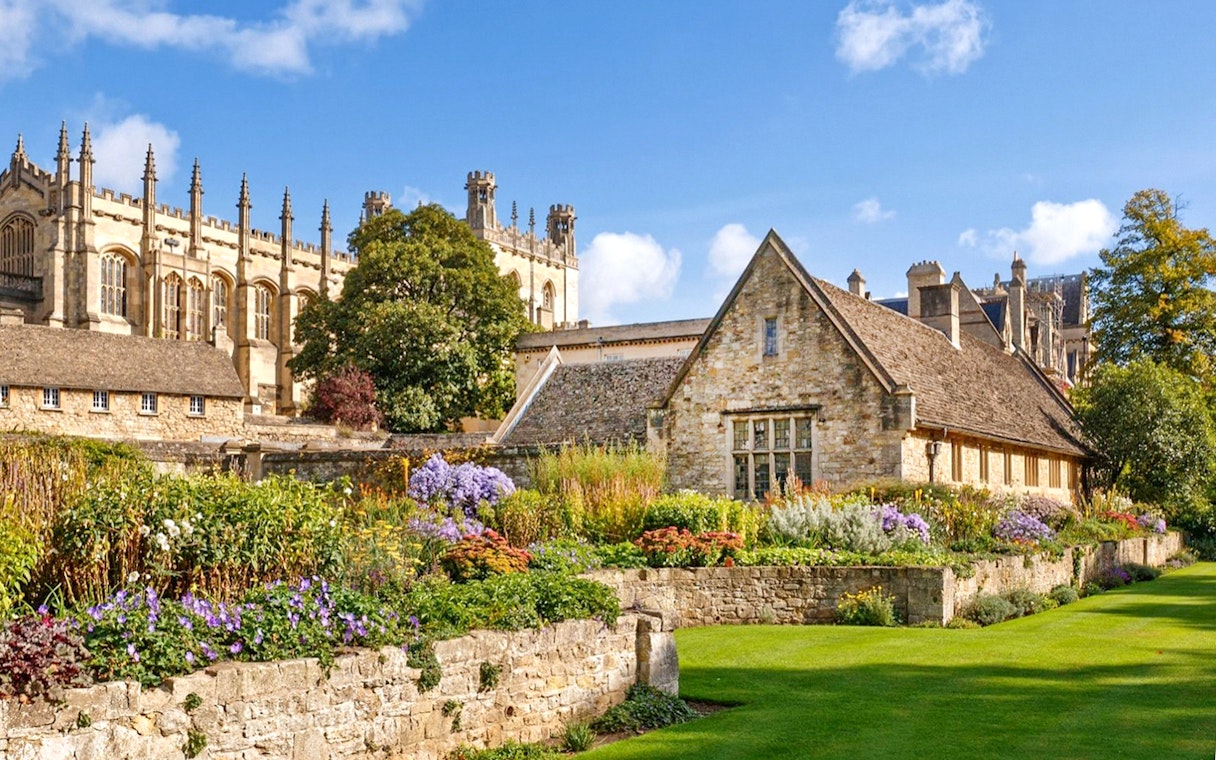 Oxford University garden with historic stone buildings and vibrant flowers.