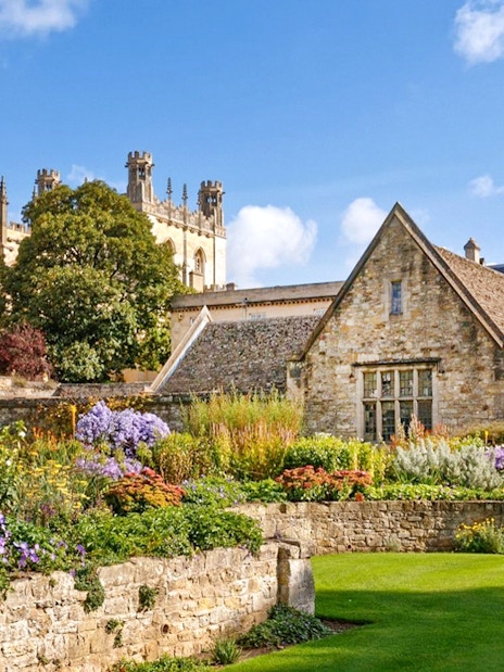 Oxford University garden with historic stone buildings and vibrant flowers.