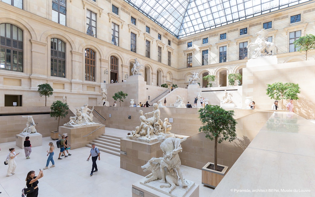 Louvre Museum interior with sculptures and visitors exploring the gallery.