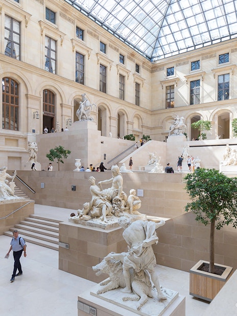 Louvre Museum interior with sculptures and visitors exploring the gallery.