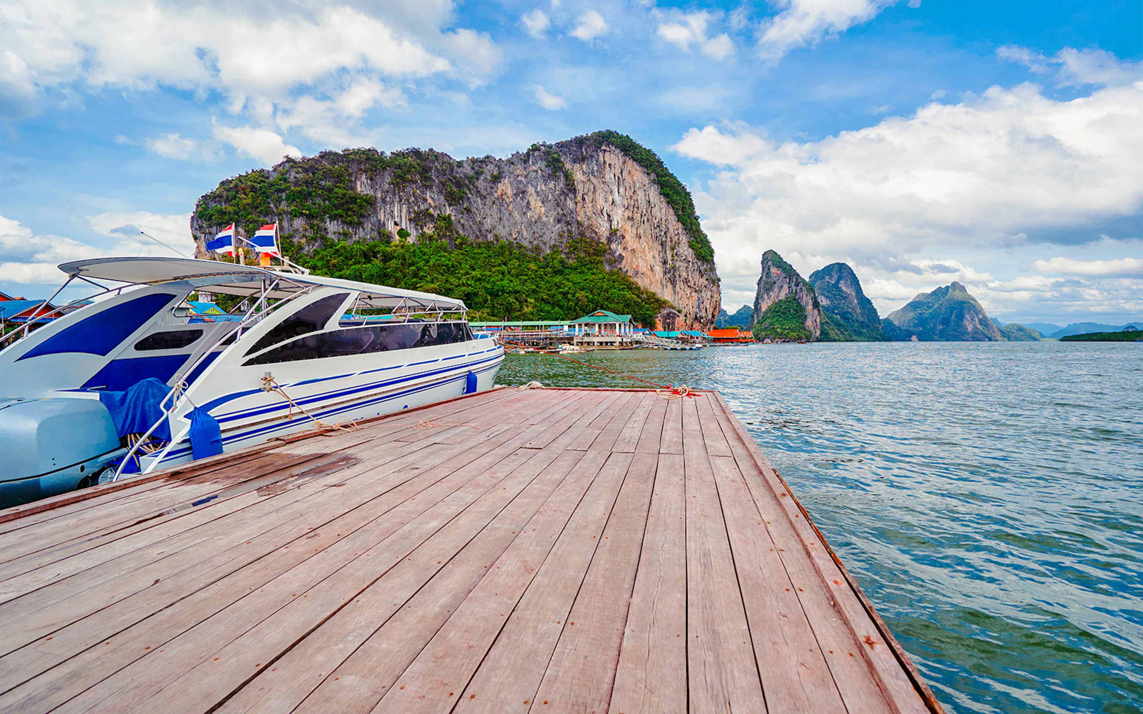 Speedboat docked at a wooden pier with limestone cliffs in the background, Thailand.