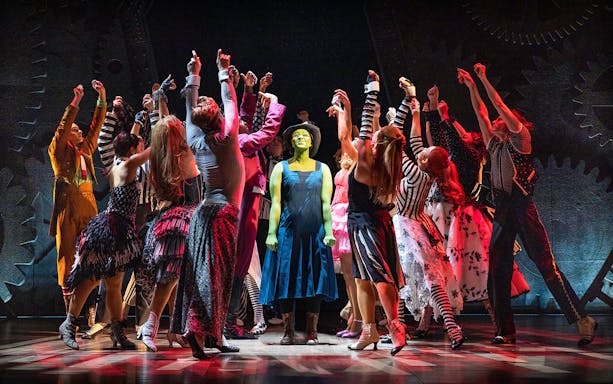 Performers in colorful costumes on stage during a scene from the musical Wicked.