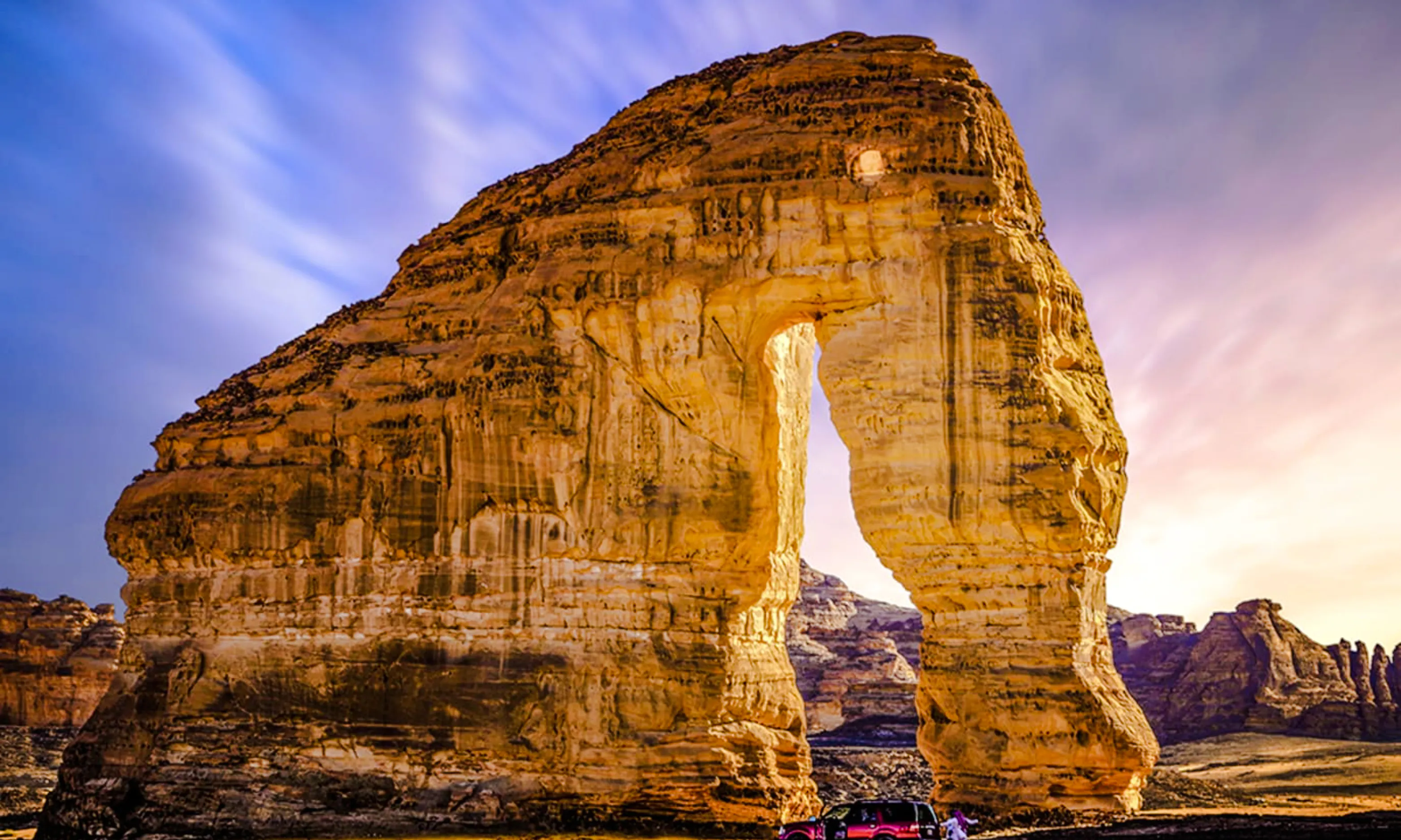Elephant Rock in AlUla, Saudi Arabia, with a car parked nearby at sunset.