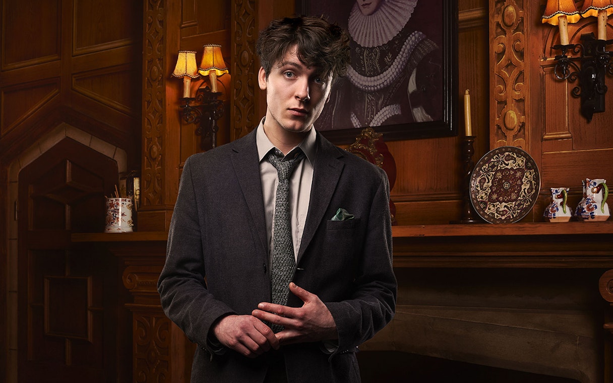 Man in a suit standing in a vintage room with ornate wood paneling, related to The Mousetrap.