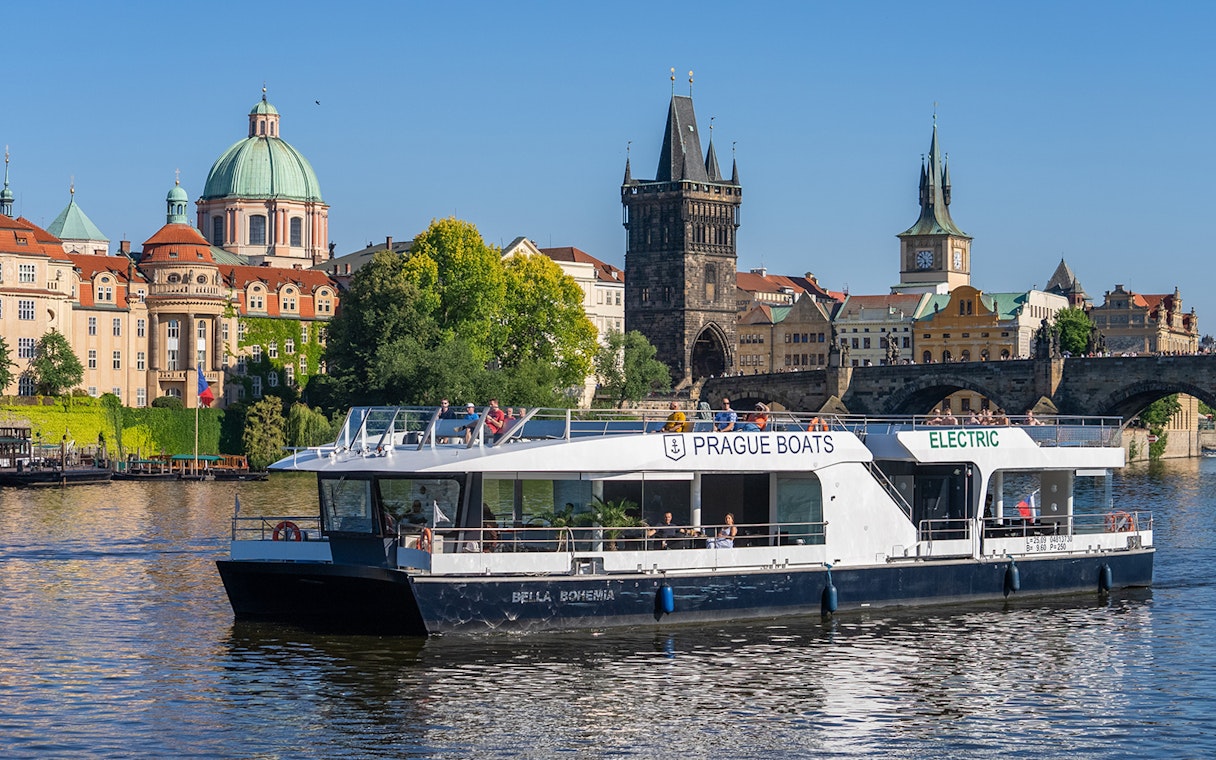 Cruise boat on Vltava River passing Charles Bridge in Prague.
