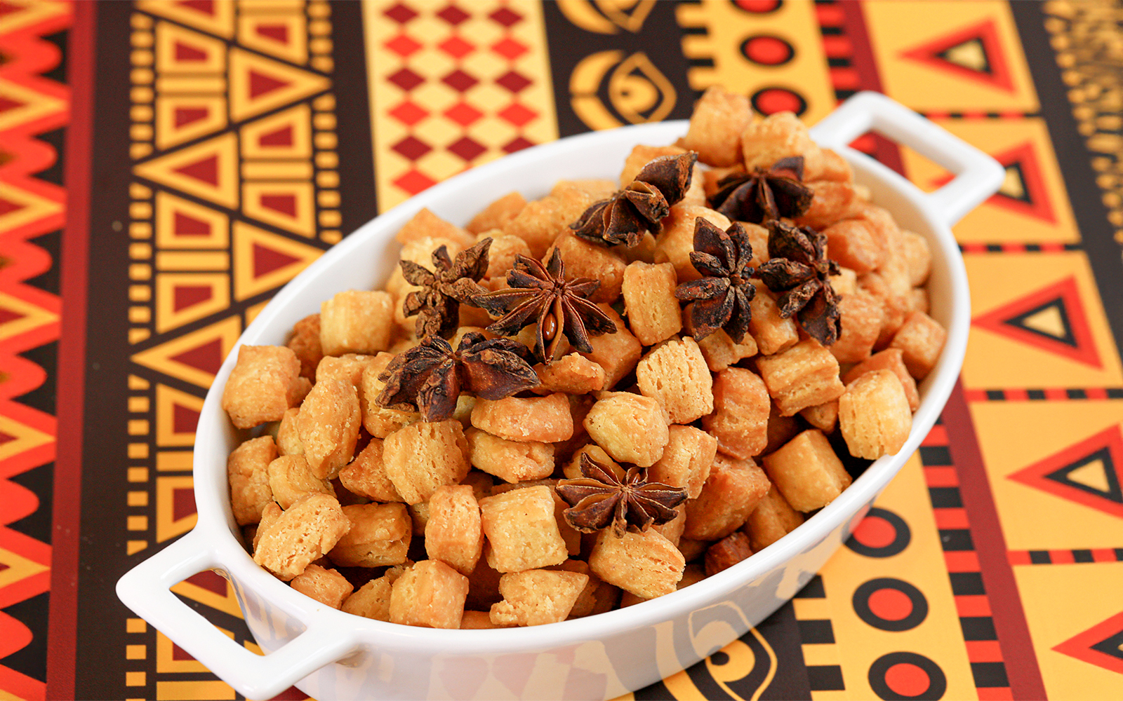 Chin Chin in a white bowl with star anise on a colorful African-patterned tablecloth.