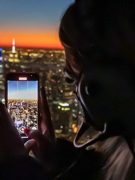 Person photographing NYC skyline at sunset from helicopter during private tour.