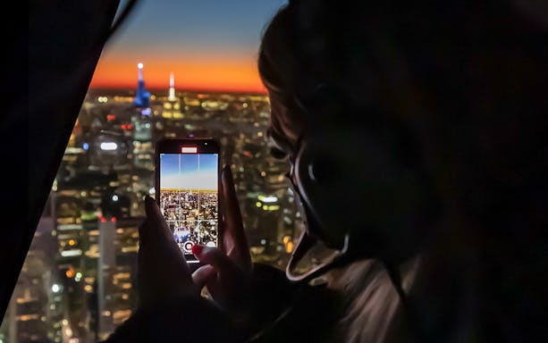 Person photographing NYC skyline at sunset from helicopter during private tour.