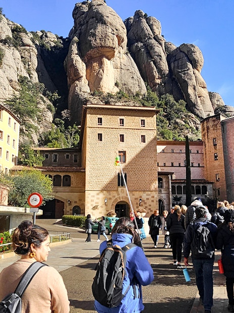 Tourists entering Montserrat Monastery with rocky mountain backdrop.