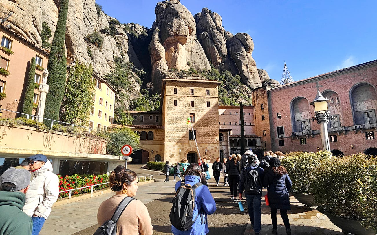 Tourists entering Montserrat Monastery with rocky mountain backdrop.