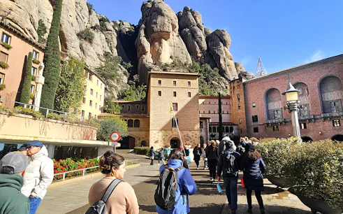 Tourists entering Montserrat Monastery with rocky mountain backdrop.
