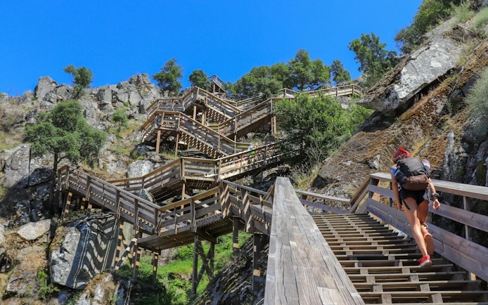 Woman ascending wooden stairs on Paiva Walkways with backpack, Portugal.