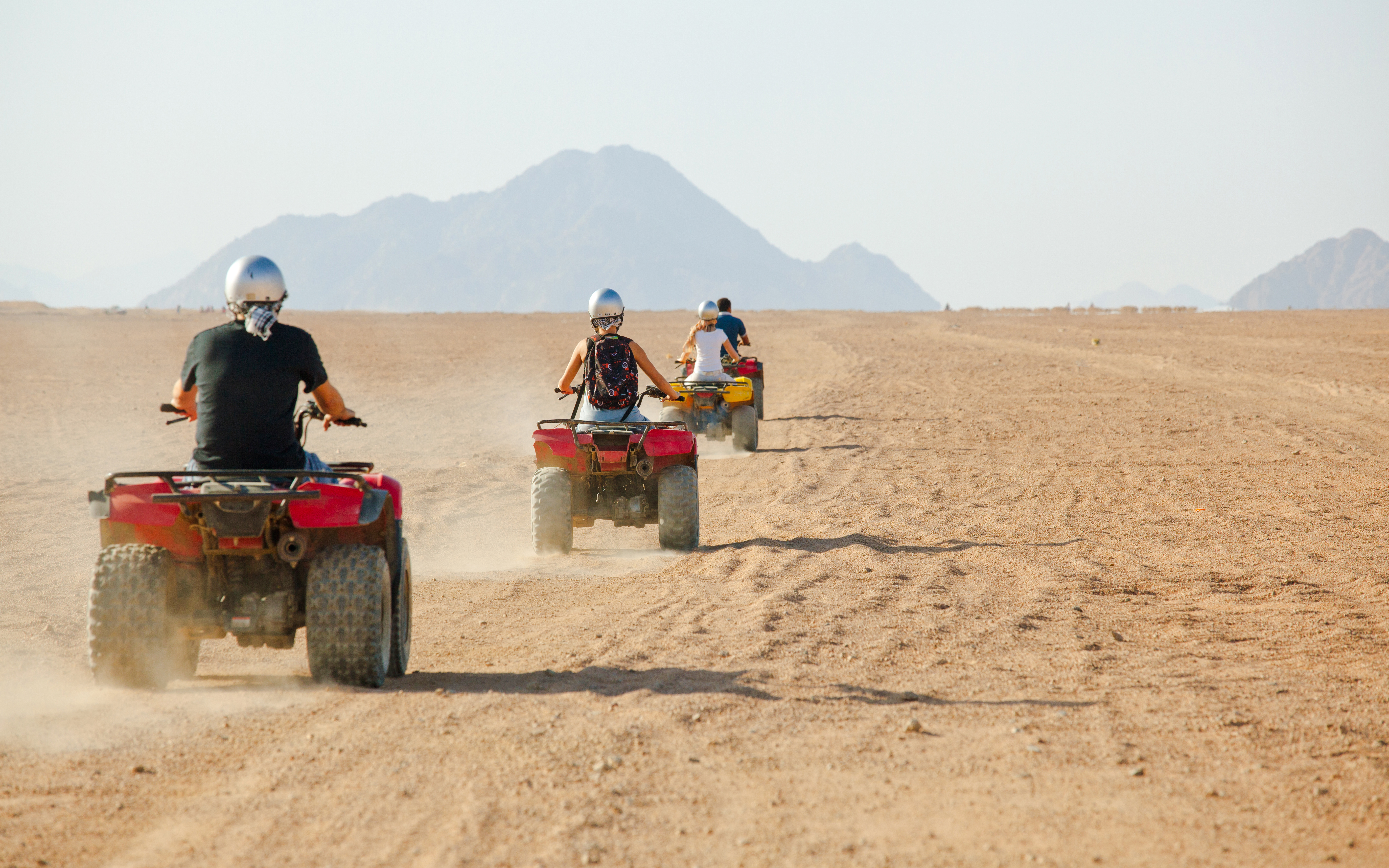 People riding quad bikes in a desert landscape with mountains in the background.