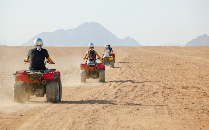 People riding quad bikes in a desert landscape with mountains in the background.