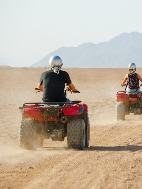 People riding quad bikes in a desert landscape with mountains in the background.