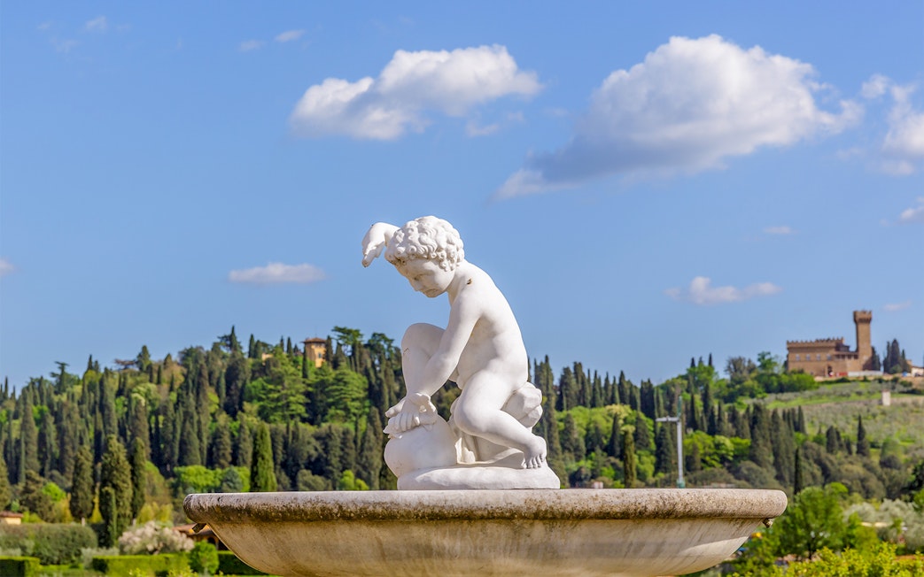 Sculpture in Boboli Gardens with lush greenery and historic architecture, Florence, Italy.