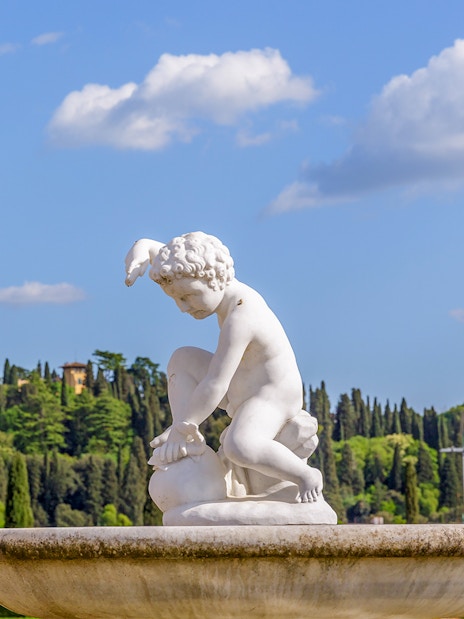 Sculpture in Boboli Gardens with lush greenery and historic architecture, Florence, Italy.