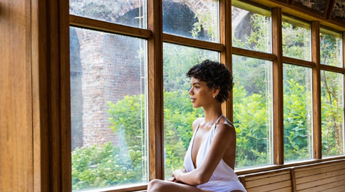 Person relaxing in a wooden sauna at QC Terme Milano, with garden view through large windows.