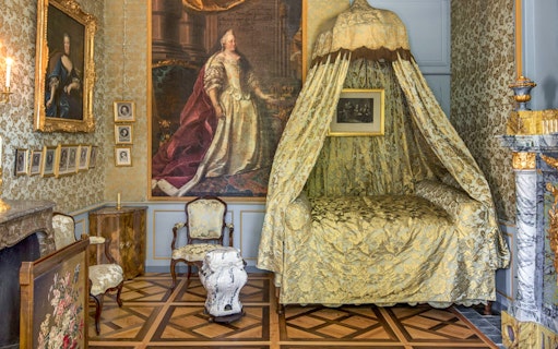 Voltaire's castle bedroom with ornate canopy bed and historical portraits.