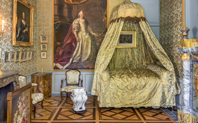 Voltaire's castle bedroom with ornate canopy bed and historical portraits.