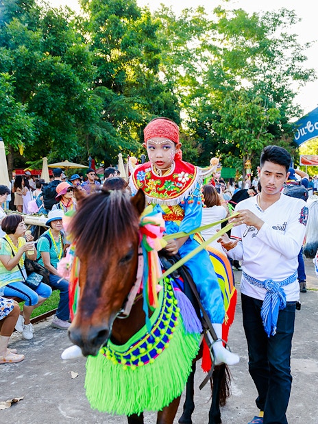 Young boy in traditional attire on a decorated horse at Chiang Mai Sky Lanterns Festival parade.