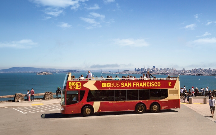 Open-top tour bus in San Francisco with city skyline and bay in the background.