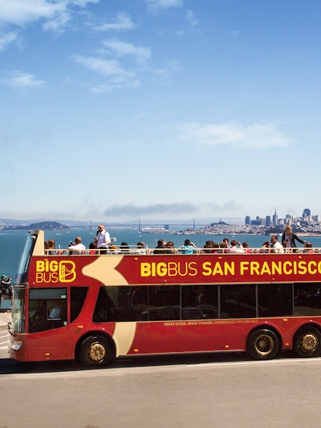 Open-top tour bus in San Francisco with city skyline and bay in the background.