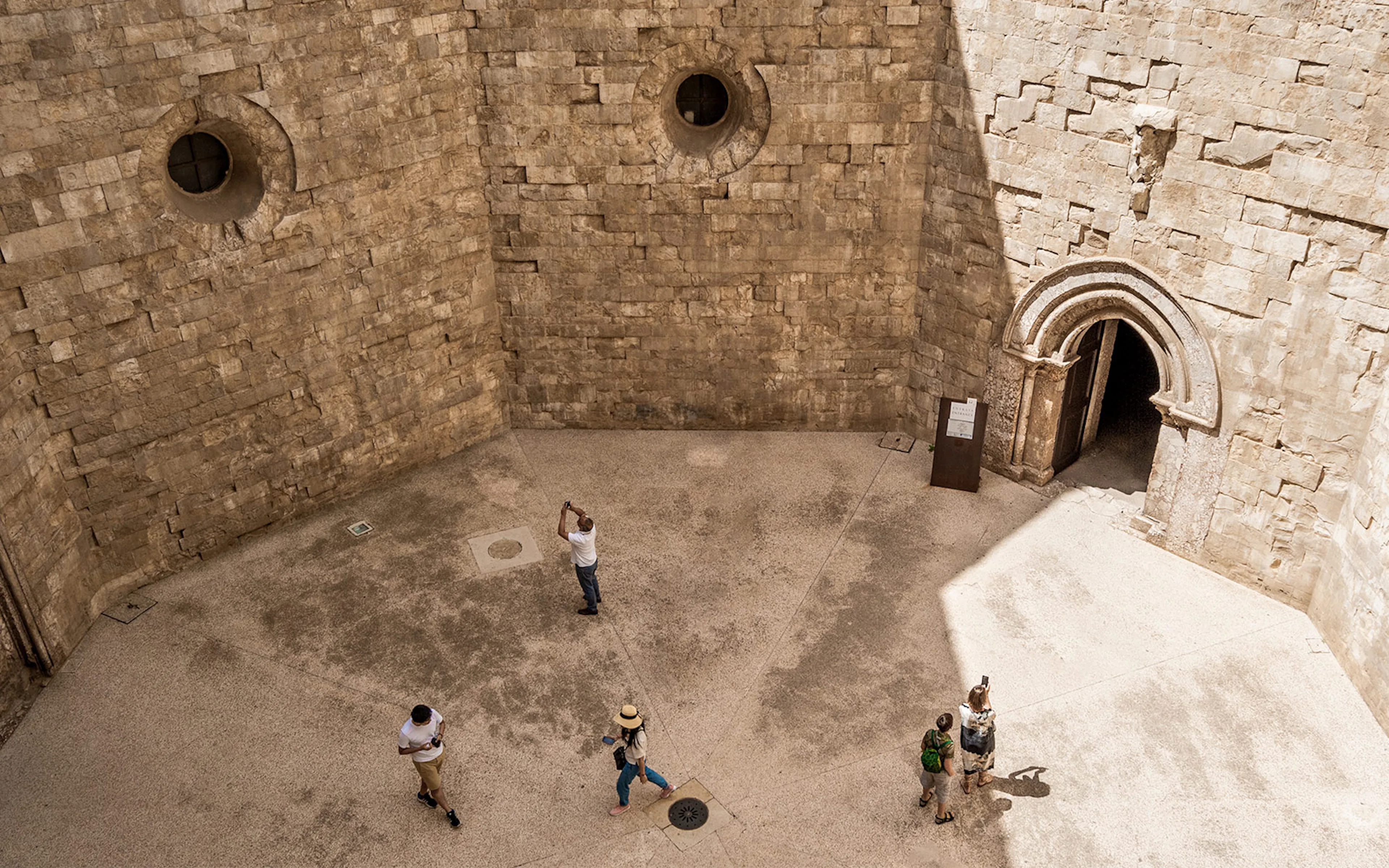 Visitors exploring the stone courtyard of Castel del Monte in Andria.