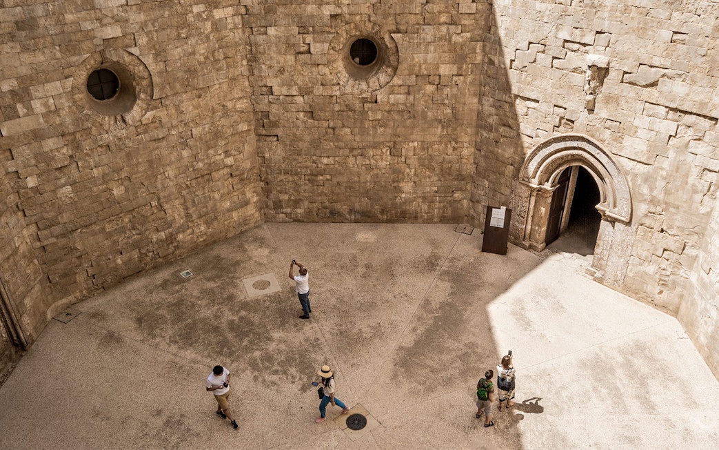 Visitors exploring the stone courtyard of Castel del Monte in Andria.