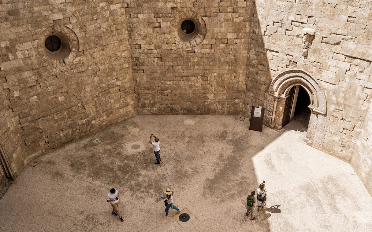 Visitors exploring the stone courtyard of Castel del Monte in Andria.
