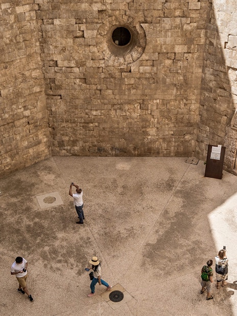 Visitors exploring the stone courtyard of Castel del Monte in Andria.