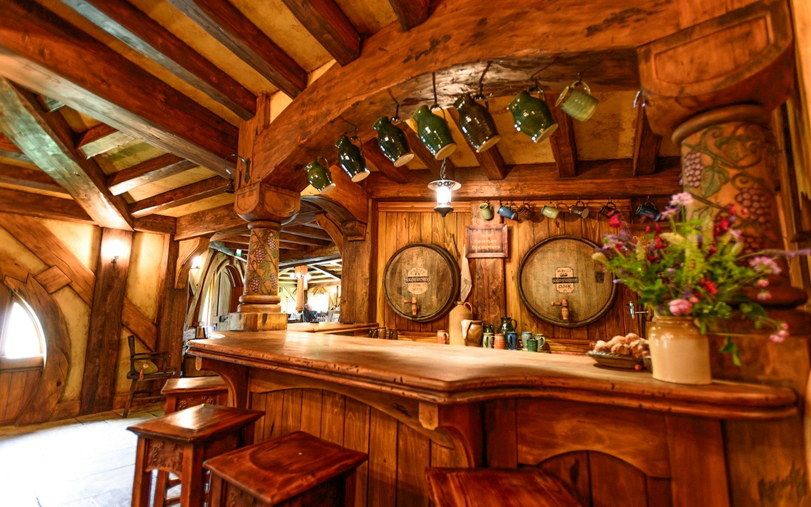 Green Dragon Inn interior with wooden bar and hanging mugs at Hobbiton movie set.