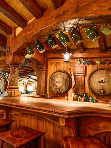 Green Dragon Inn interior with wooden bar and hanging mugs at Hobbiton movie set.