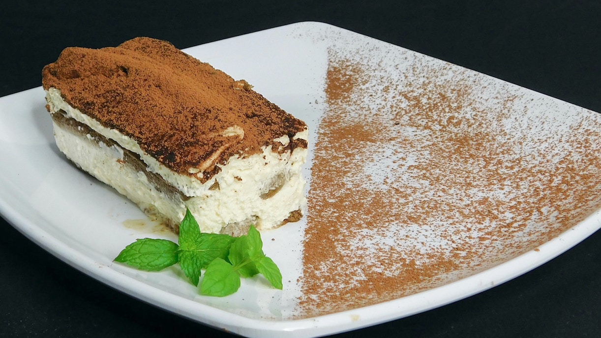 Tiramisù slice on a plate with cocoa powder, part of a cooking class in Florence.