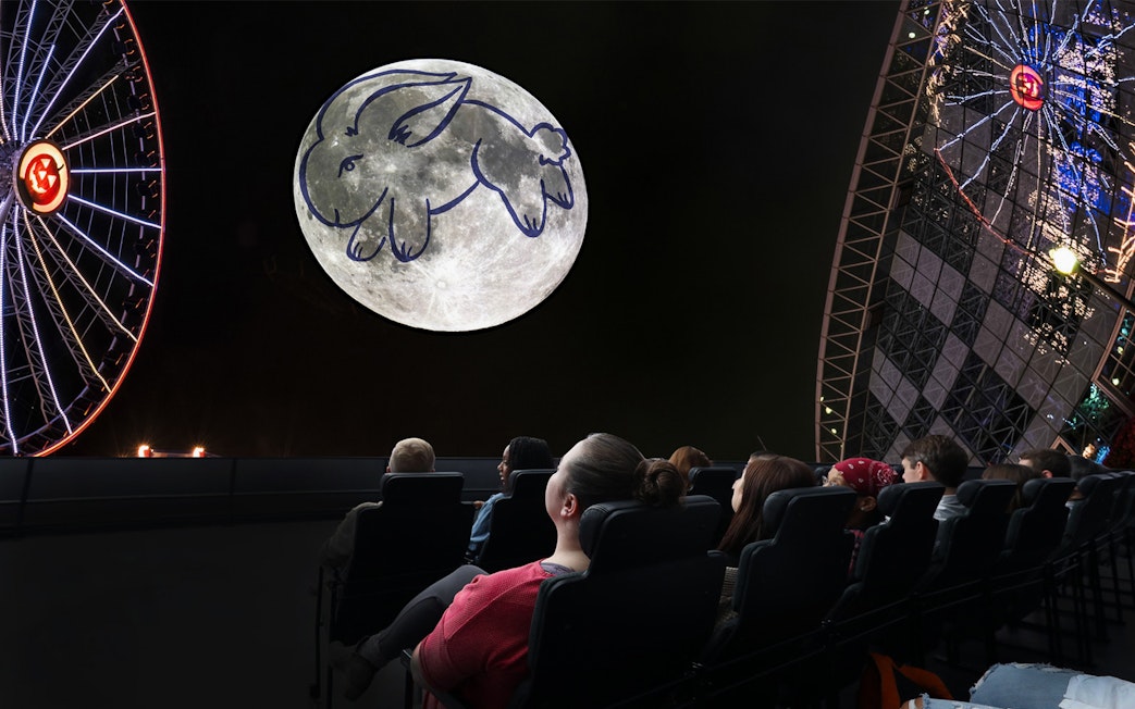 Visitors watching a moon projection with a rabbit drawing at a Chicago planetarium.