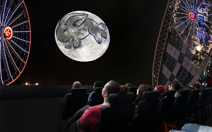 Visitors watching a moon projection with a rabbit drawing at a Chicago planetarium.