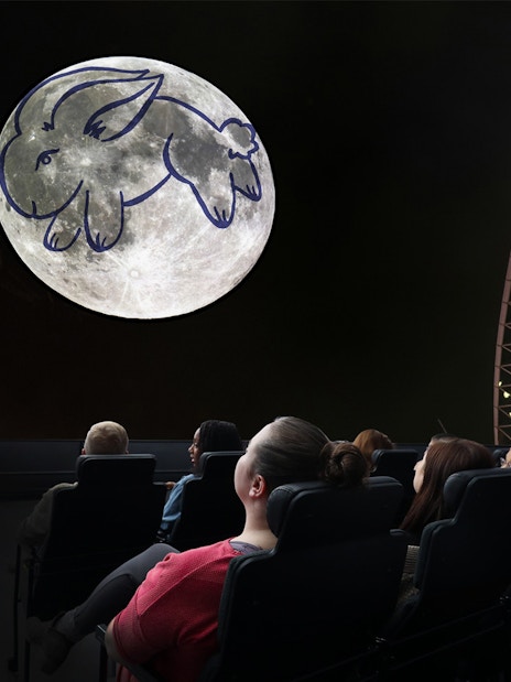 Visitors watching a moon projection with a rabbit drawing at a Chicago planetarium.