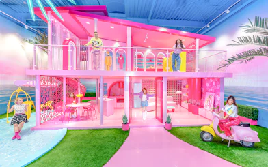 Barbie Dreamhouse experience with visitors exploring vibrant pink rooms and outdoor swing.