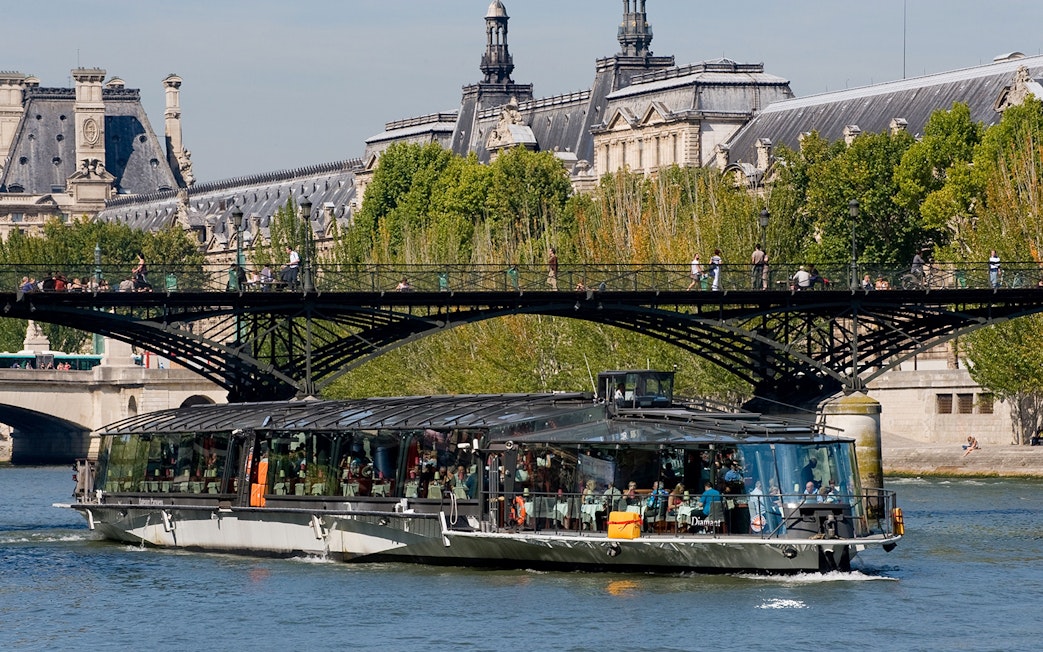 Seine River cruise boat near Paris bridge, with passengers dining, starting at Eiffel Tower.