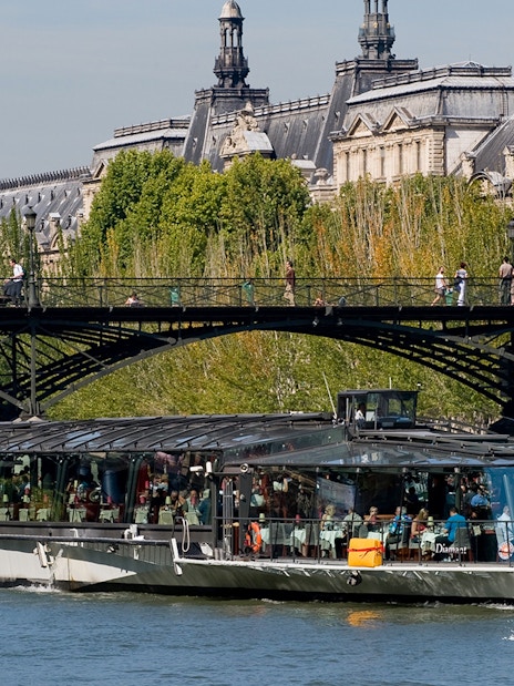 Seine River cruise boat near Paris bridge, with passengers dining, starting at Eiffel Tower.