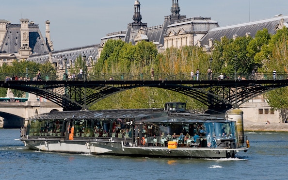 Seine River cruise boat near Paris bridge, with passengers dining, starting at Eiffel Tower.