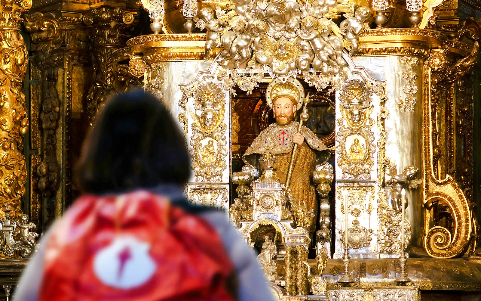 Pilgrim with backpack facing Apostle Santiago statue inside Santiago de Compostela Cathedral.