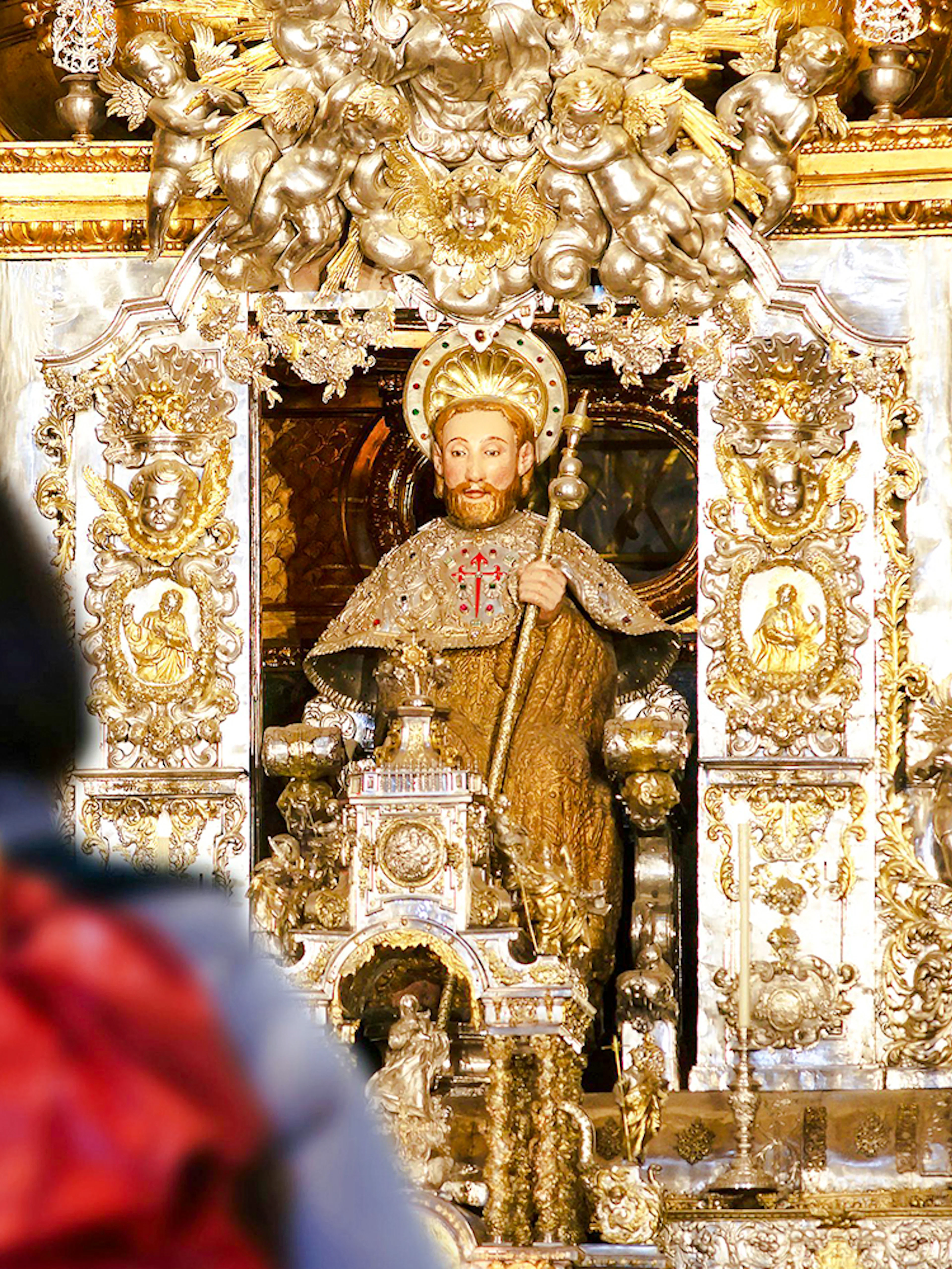 Pilgrim with backpack facing Apostle Santiago statue inside Santiago de Compostela Cathedral.